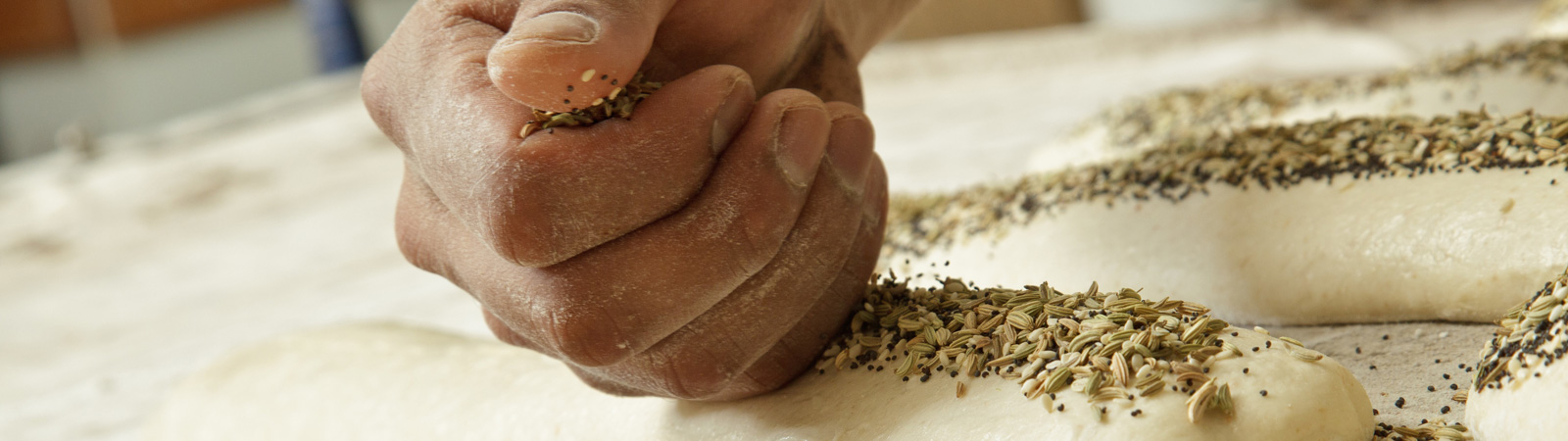 Hand spreading seeds on top of bread dough.